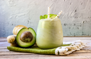 Lasi vihreää avokado-banaanismoothieta, jonka vieressä kokonainen ja puolikas avokado sekä banaaneja.