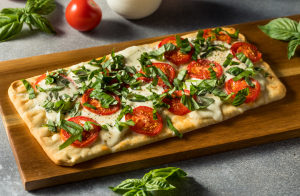 Kasvispizza tai flatbread, jossa on tuoreita tomaatteja, mozzarellaa ja silputtua basilikaa puisella tarjoilualustalla.