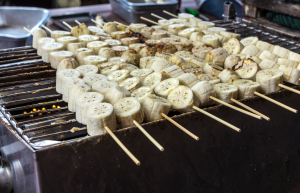 Banaanin paloja tikussa ritilägrillissä kypsymässä, grillaus käynnissä usean tikun voimin.