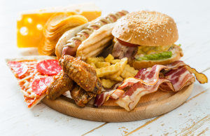 Lautasella erilaisia runsasrasvaisia pikaruokia, kuten hampurilainen, pekoni, ranskalaiset, hot dog ja pizzapala.