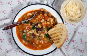 Paksu tomaattipohjainen keitto, jossa papuja, pastaa ja vihanneksia, tarjoiltuna paahdetun leipäviipaleen kanssa.