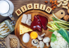 Pöydällä eri biotiinipitoisia ruoka-aineita, kuten maksa, kananmuna, juusto, maito, sardiinit, pavut, kaali, sienet ja pähkinät. Keskellä puiset palikat muodostavat sanan "Biotin".