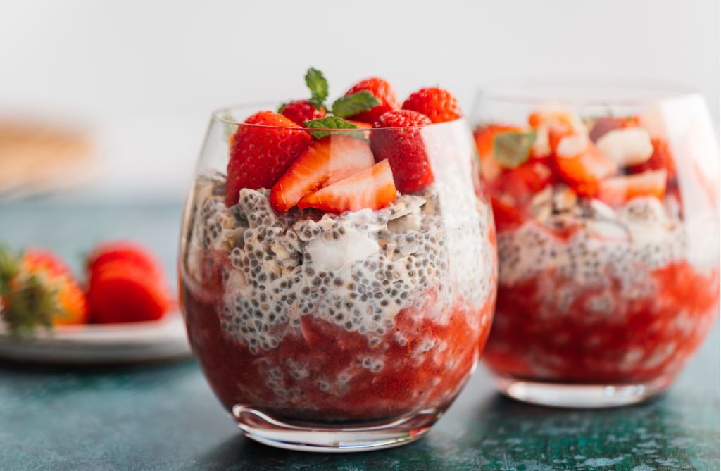 Mansikka-chia-vanukas tarjoiltuna lasissa kerroksittain. Alimpana mansikkasose, keskellä turvonnut chia-vanukas ja päällä tuoreita mansikoita sekä mintunlehtiä.