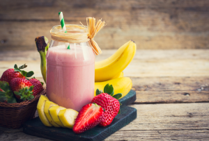 Vaaleanpunainen mansikka-banaanismoothie lasipurkissa, vieressä tuoreita mansikoita ja banaaneja.