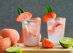 Kaksi lasillista persikkapohjaista mocktailia jääpaloilla, koristeltu tuoreilla persikkaviipaleilla ja limeillä.