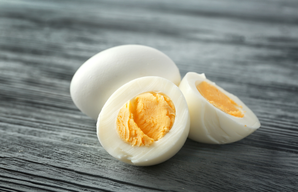 Keitetty kananmuna ja puoliksi leikattuja kananmunia puupinnalla.