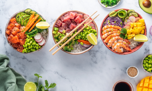 Kolme värikästä sushibowlia limelohkoilla koristeltuna; kulhoissa lohta, tonnikalaa, katkarapuja, mangoa, avokadoa, edamamea ja kasviksia.