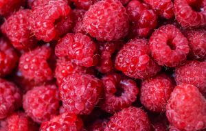 Lähikuva tuoreista tai pakastetuista vadelmista, tiiviisti pinottuna kirkkaanpunaisena marjamassana.