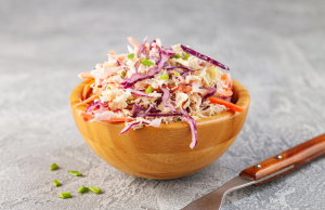 Värikäs coleslaw-salaatti puukulhossa, mukana punakaalia, porkkanaa ja vihreää sipulia.