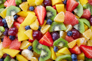 Värikäs lähikuva pilkotuista hedelmistä, kuten kiivistä, mansikasta, mangosta, appelsiinista, greipistä, banaanista, rypäleistä ja mustikoista.