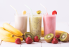 Kolme smoothielasia banaanilla, kiivillä ja mansikalla koristeltuna, edessä tuoreita hedelmiä.