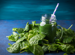Ylhäältä päin kuvattu vihreä pinaattismoothie lasipurkissa, ympärillä pinaatinlehtiä