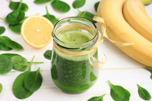 Vihreä pinaattismoothie lasipurkissa, ympärillä sitruuna, banaaneja ja pinaatinlehtiä