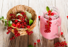 Punertava smoothie lasipurkissa, jonka päällä punaherukoita ja mintunlehtiä. Vieressä pieni kori täynnä tuoreita punaherukoita. Taustalla vanha puupöytä.