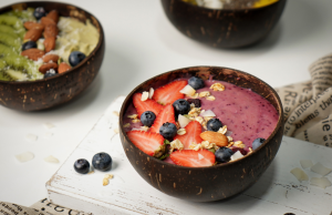 Kookoskulhossa tarjoiltu smoothiebowl, jossa mustikoita, mansikoita, mysliä ja manteleita.