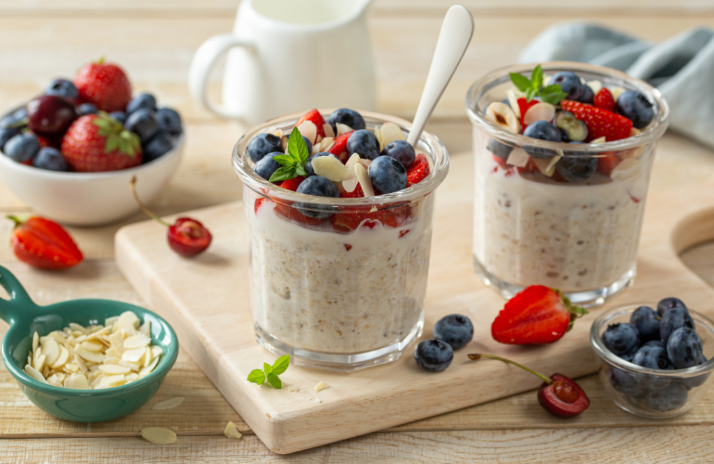 Kaksi lasipurkillista tuorepuuroa, joissa päällä mustikoita, mansikoita, mantelilastuja ja tuoretta minttua. Taustalla tuoreita marjoja ja pieni kannu.