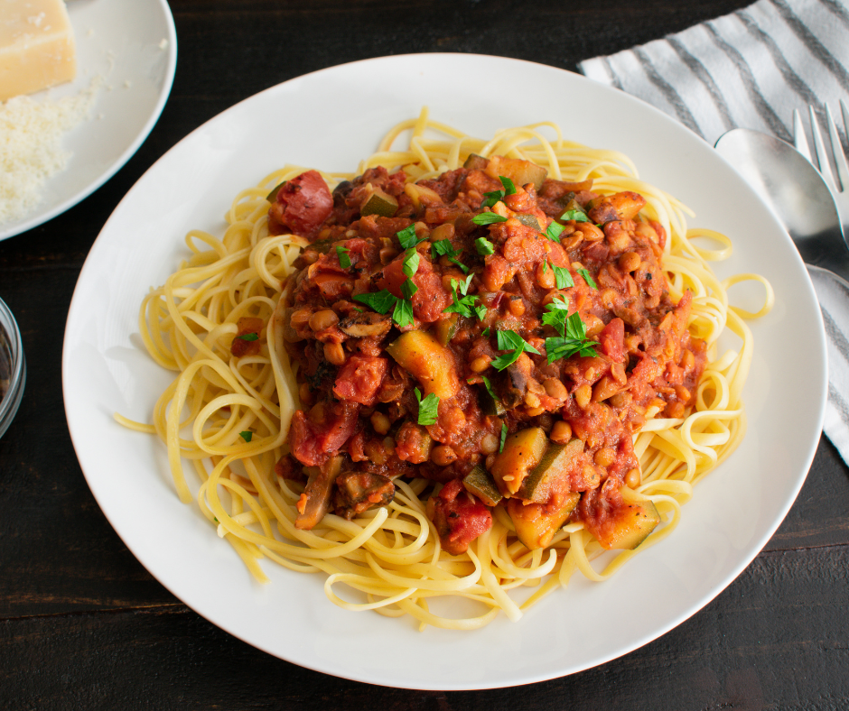 Kuva linssibolognesesta spagetin kanssa. Annos on valkoisella lautasella tummalla pöydällä.