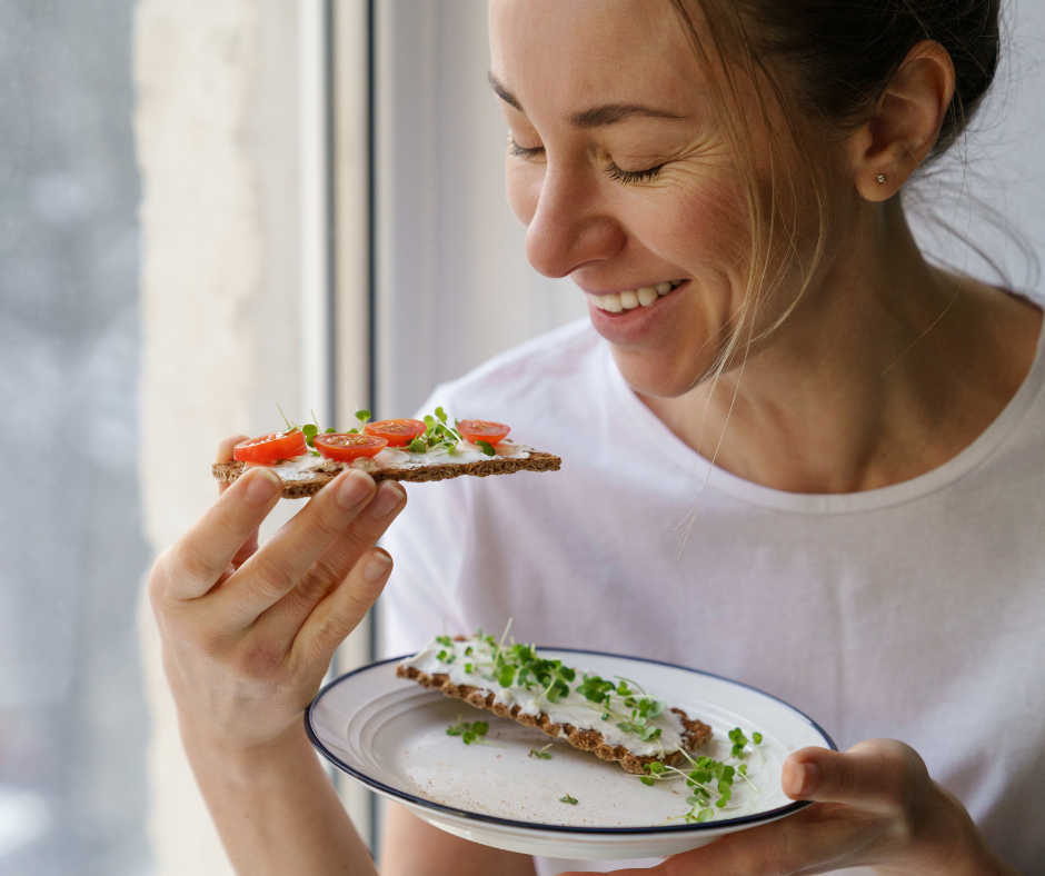 Kuvassa nainen syö aamiaiseksi kaksi näkkileipää, joissa on tuorejuustoa ja kasviksia päällä.