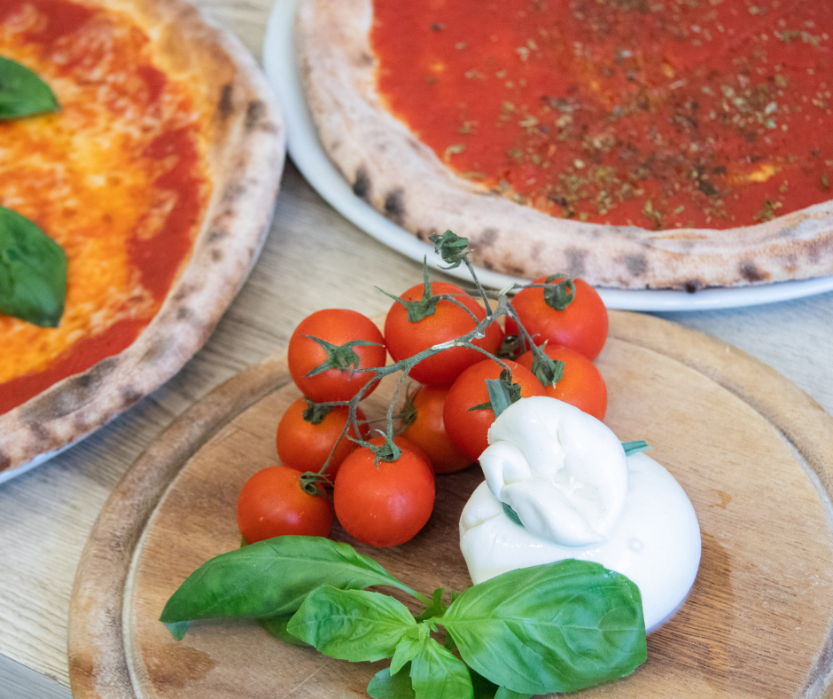 Kuvassa tehdään pizzaa, lautasilla on kaksi pizzaa ja leikkuulaudalla mozzarellaa, tomaattia ja basilikaa. Pizzaperjantai sopii osaksi 80/20 ruokavaliota.