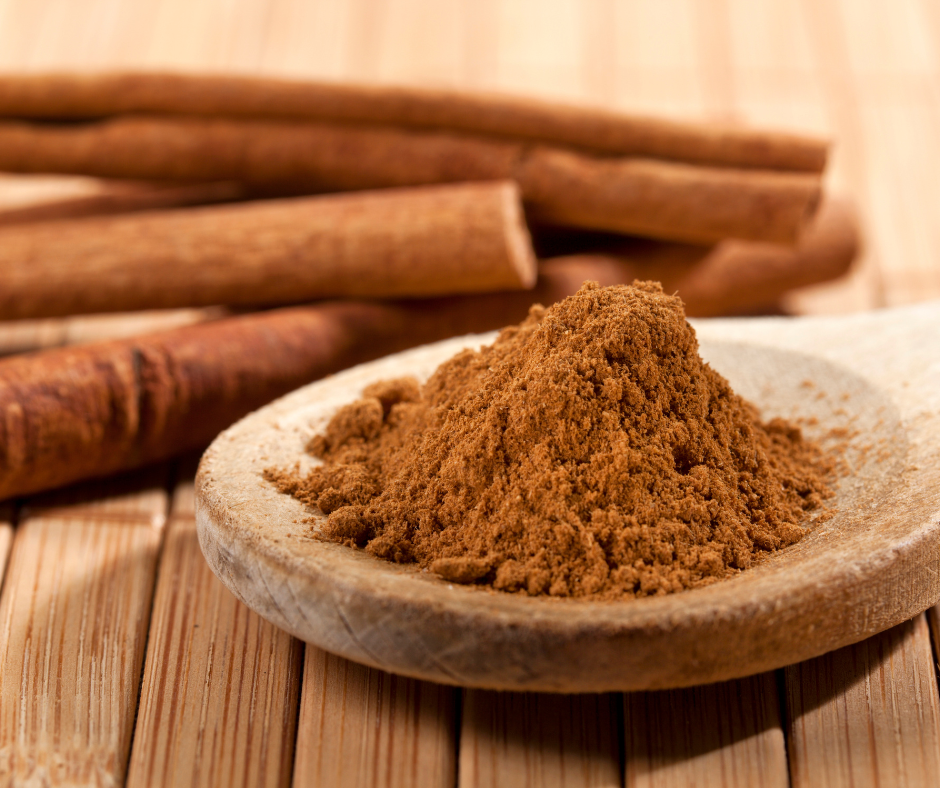 Kuvassa jauhettua kanelia puulusikassa. Lisäksi taustalla kokonaisia kanelitankoja.