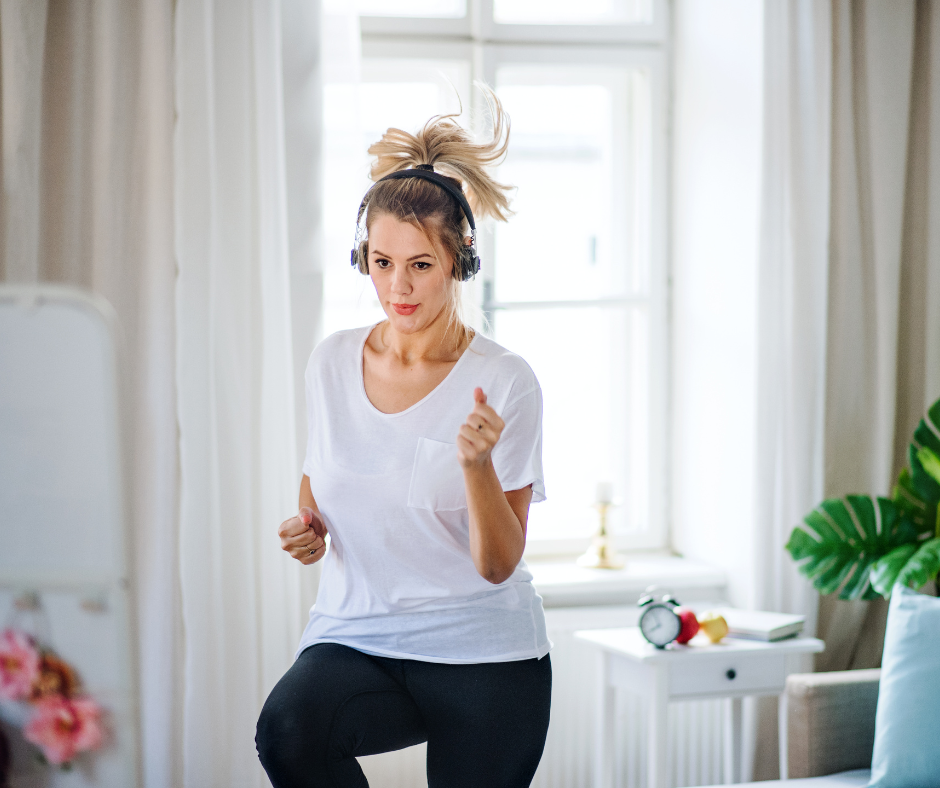 Kuvassa nainen jumppaa olohuoneessa kuulokkeet päässään. 