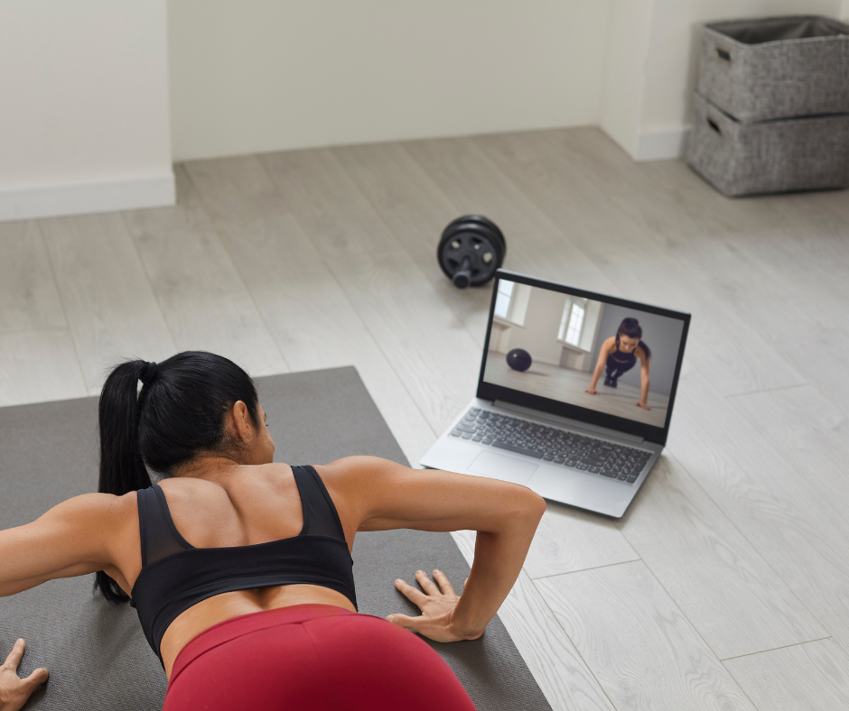 Kuvassa nainen tekee lihaskuntotreeniä kotonaan ja katsoo tietokoneelta ohjeita samalla punnerrusasennossa.