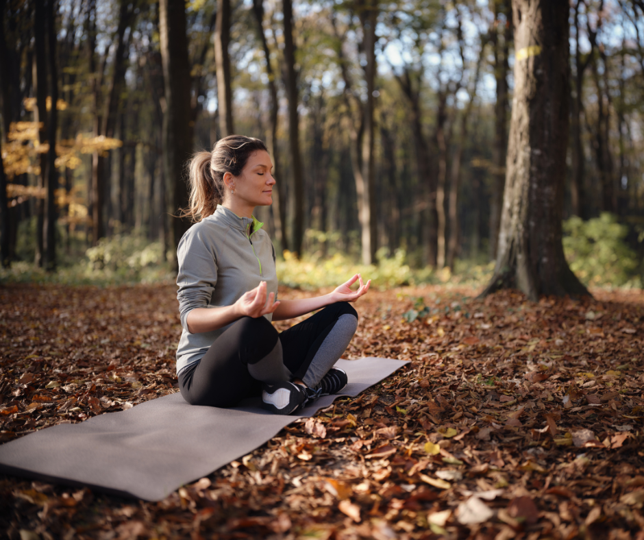 Kuvassa nainen meditoi syksyisessä maastossa jumppamaton päällä.