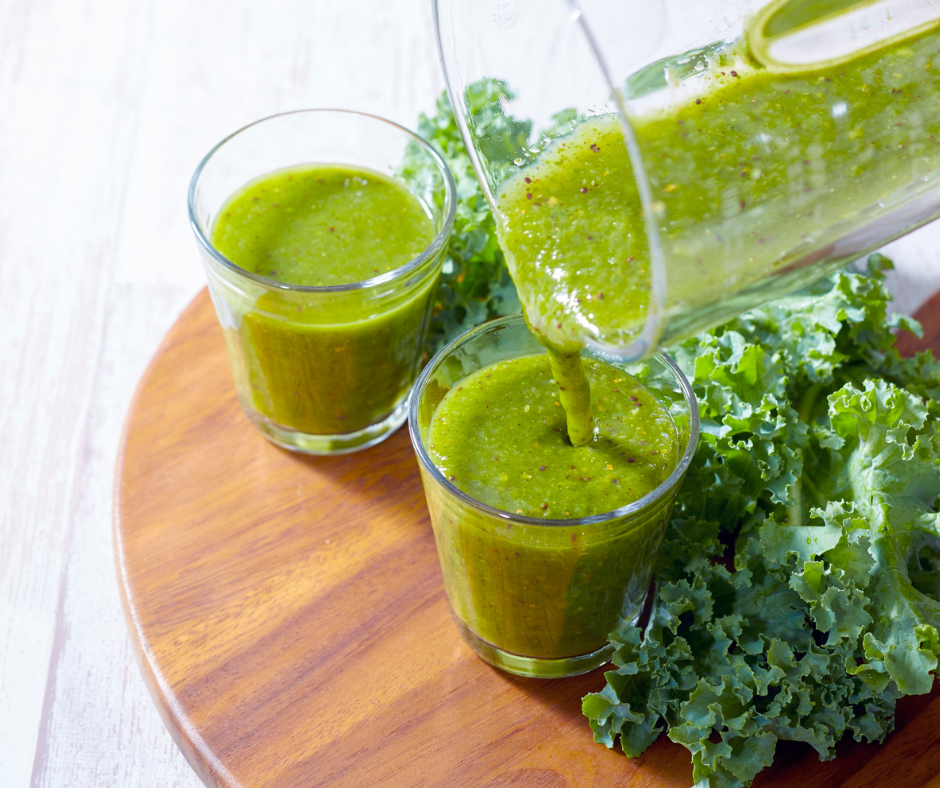 Kuvassa detox-kuuriin sopiva vihersmoothie. Smoothieta on kahdessa lasissa puisen laudan päällä. Lisäksi laudalla on lehtikaalia.