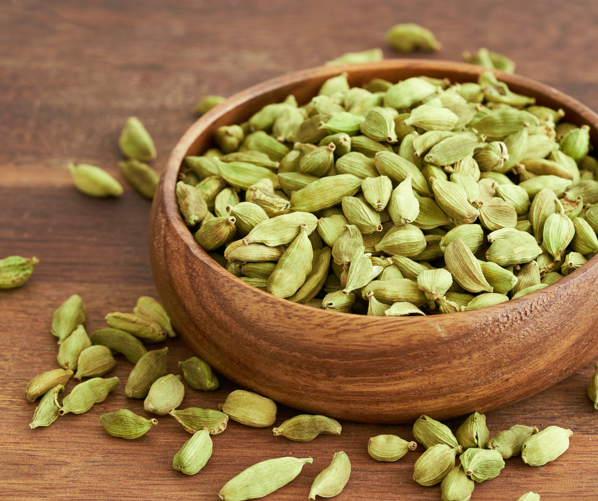 Kuvassa ruskeassa kulhossa ja sen ympärillä tuoretta kardemummaa.