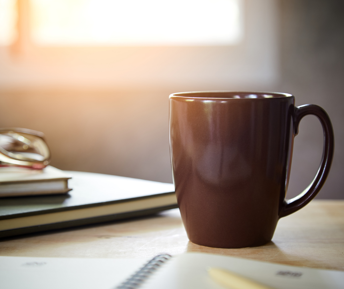 Kuvassa kuppi kahvia. Taustalla näkyy myös tietokone.