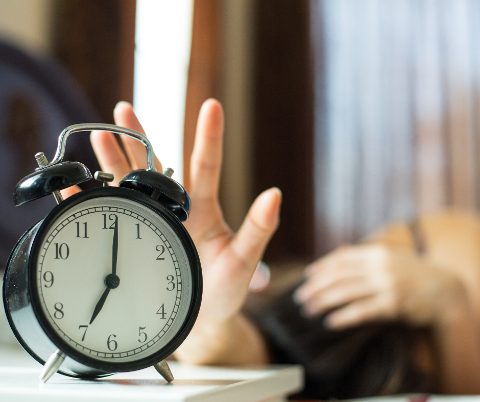 Kuvassa herätyskello, jonka herätys painetaan kädellä pois. 