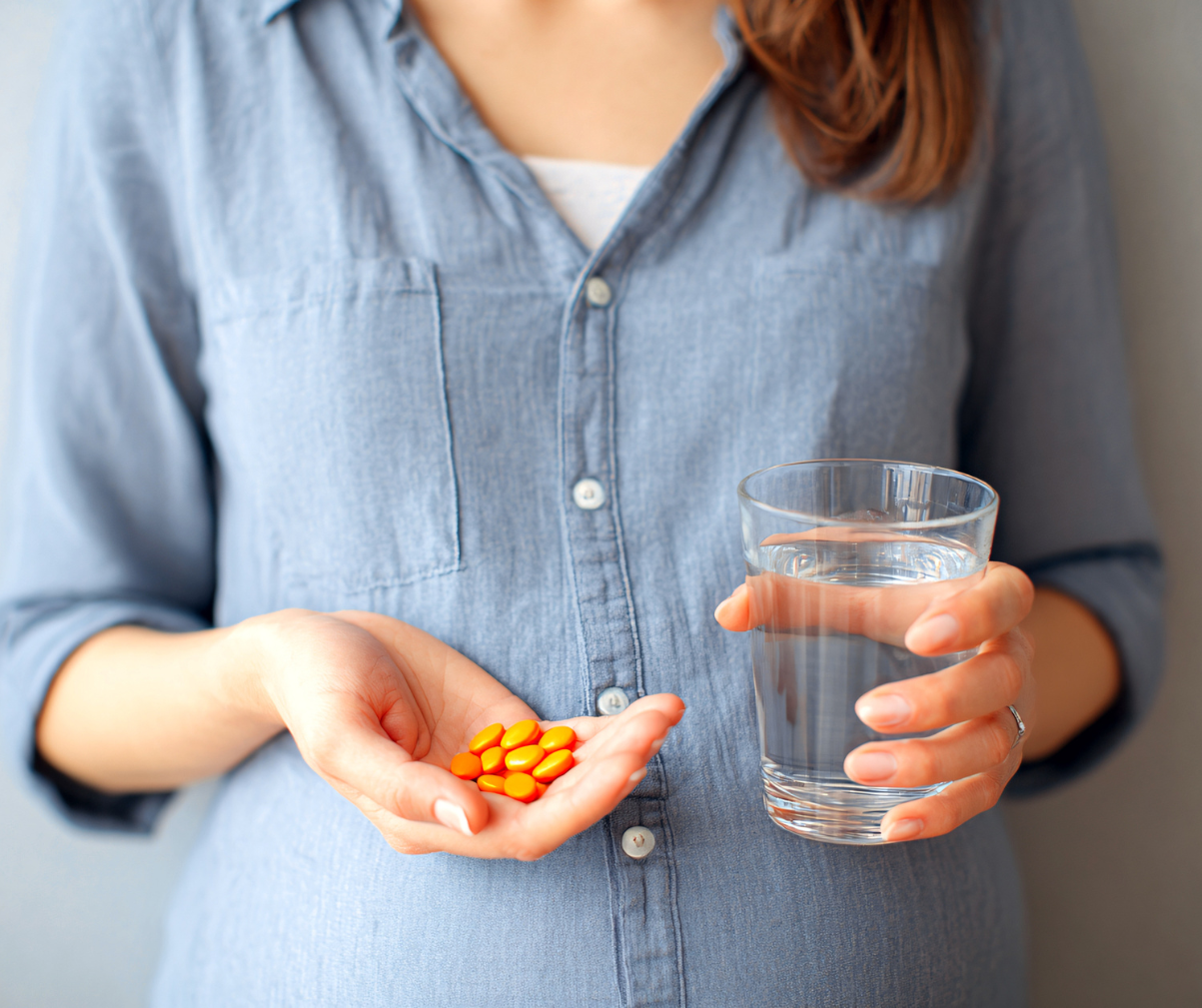 Kuvassa naisella on kädessä ravintolisäkapseleita ja toisessa kädessä vesilasi.