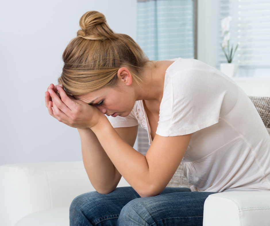 Kuvassa nainen joka on stressaantunut ja uupunut. Hän istuu sohvalla pää käsiin painautuneena.