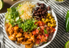 Kuvassa burrito bowl, jossa riisiä, kanaa, mustapapuja, maissia, tomaattia, juustoraastetta ja korianteria