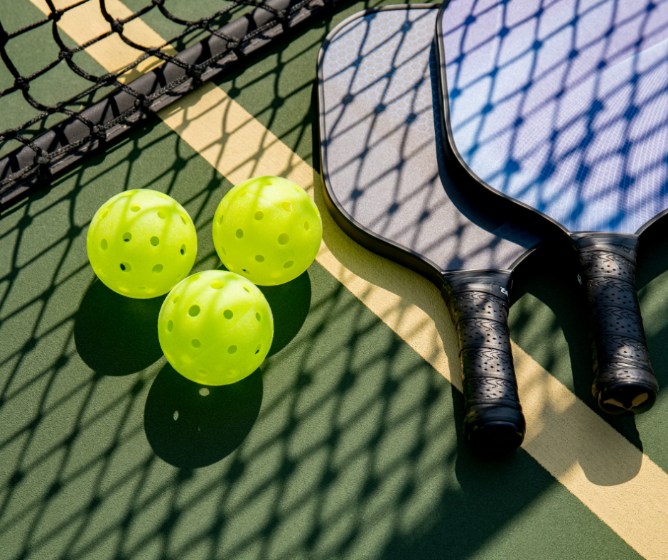 Kaksi pickle-ball mailaa kentällä, joiden vieressä on kolme pickleball-palloa