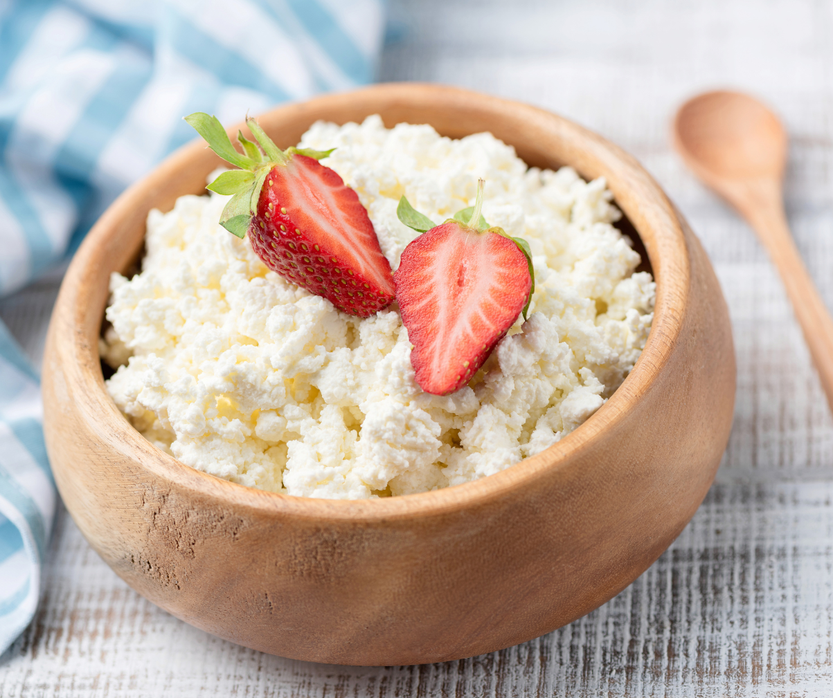 Kuvassa puisessa kulhossa raejuustoa, jossa päällä mansikoita