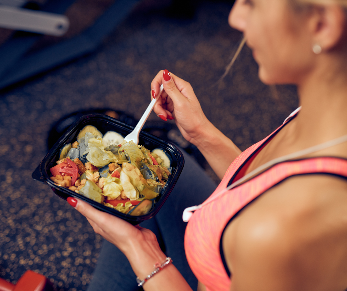 Kuvassa nainen syö proteiinipitoista ateriaa kuntosalilla