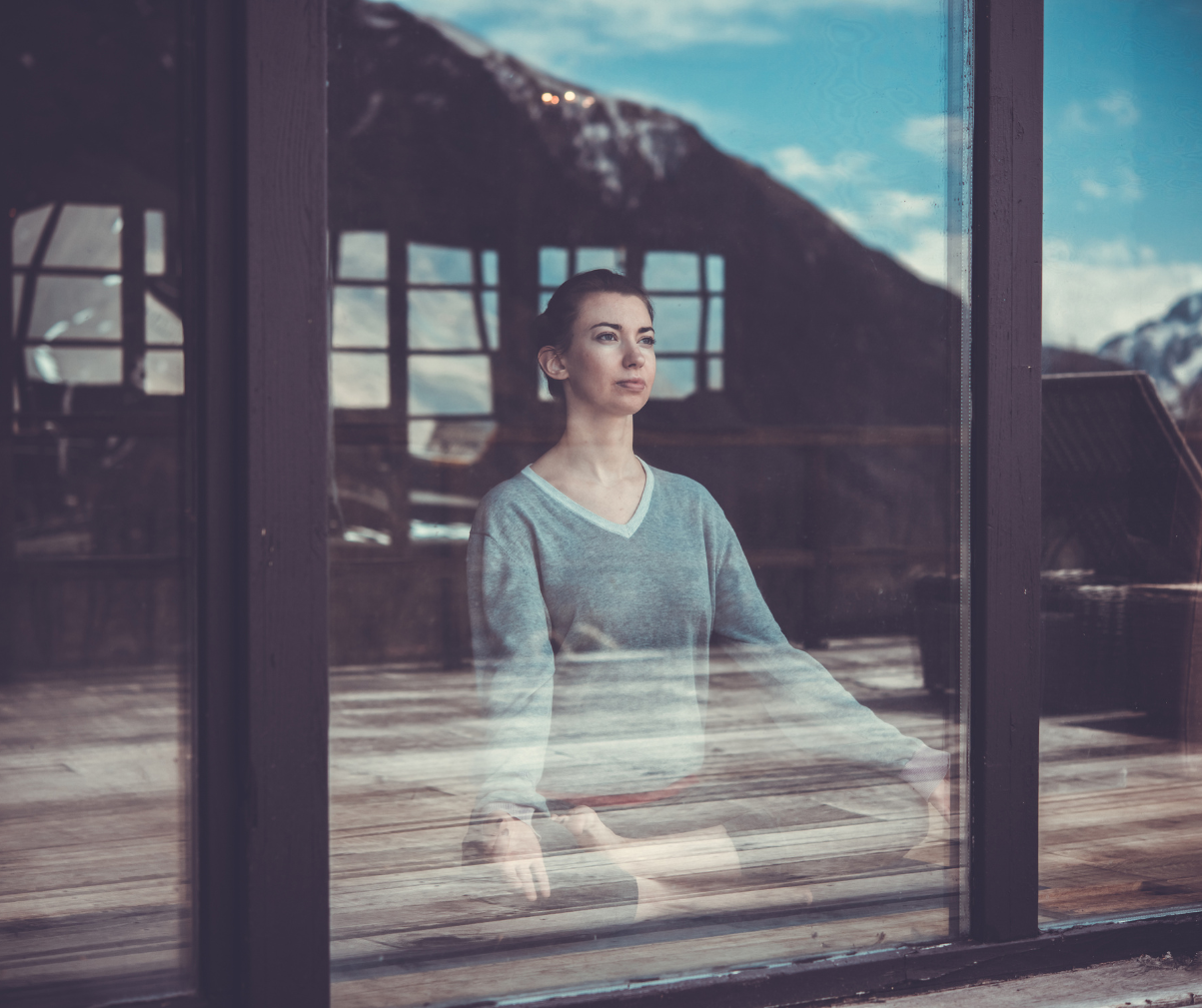 Kuvassa nainen istuu joogaistunnassa ikkunan edessä katsellen ulos
