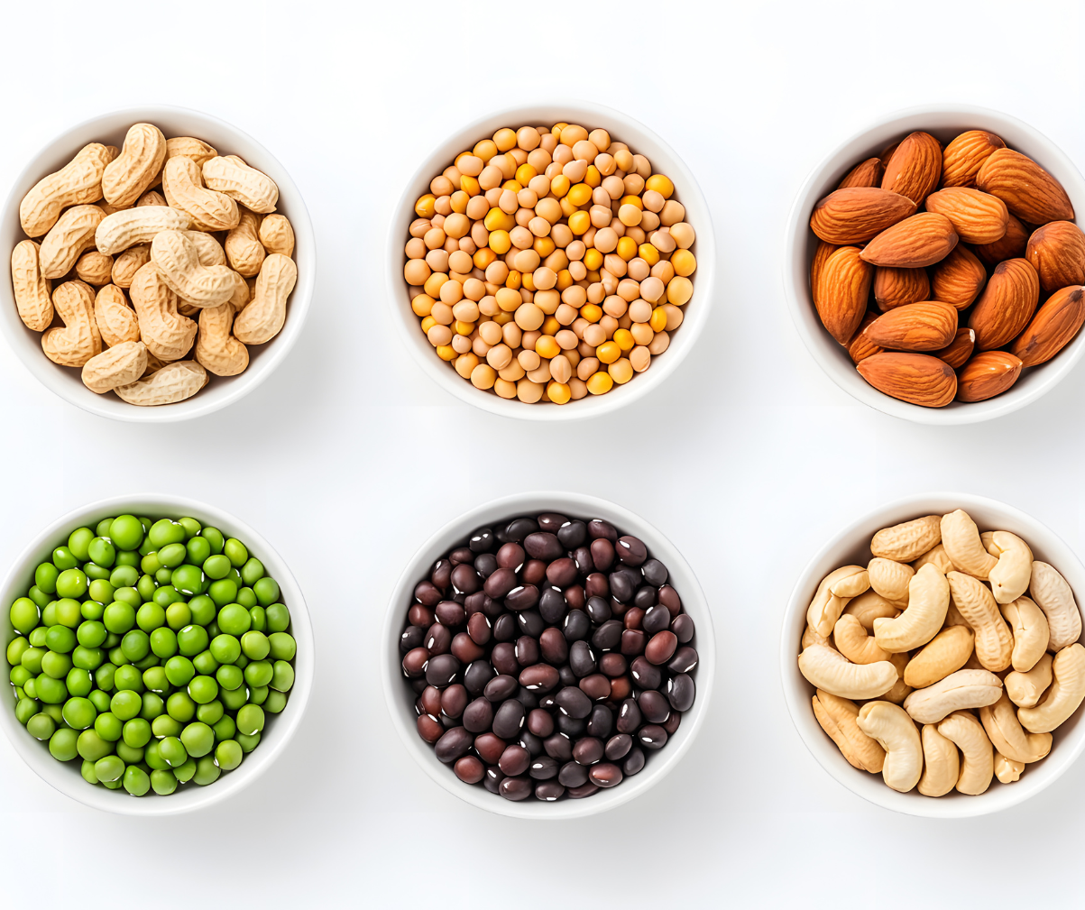Kuvassa erilaisia palkokasveja kuten herneitä, papuja ja pähkinöitä valkoisissa kupeissa.