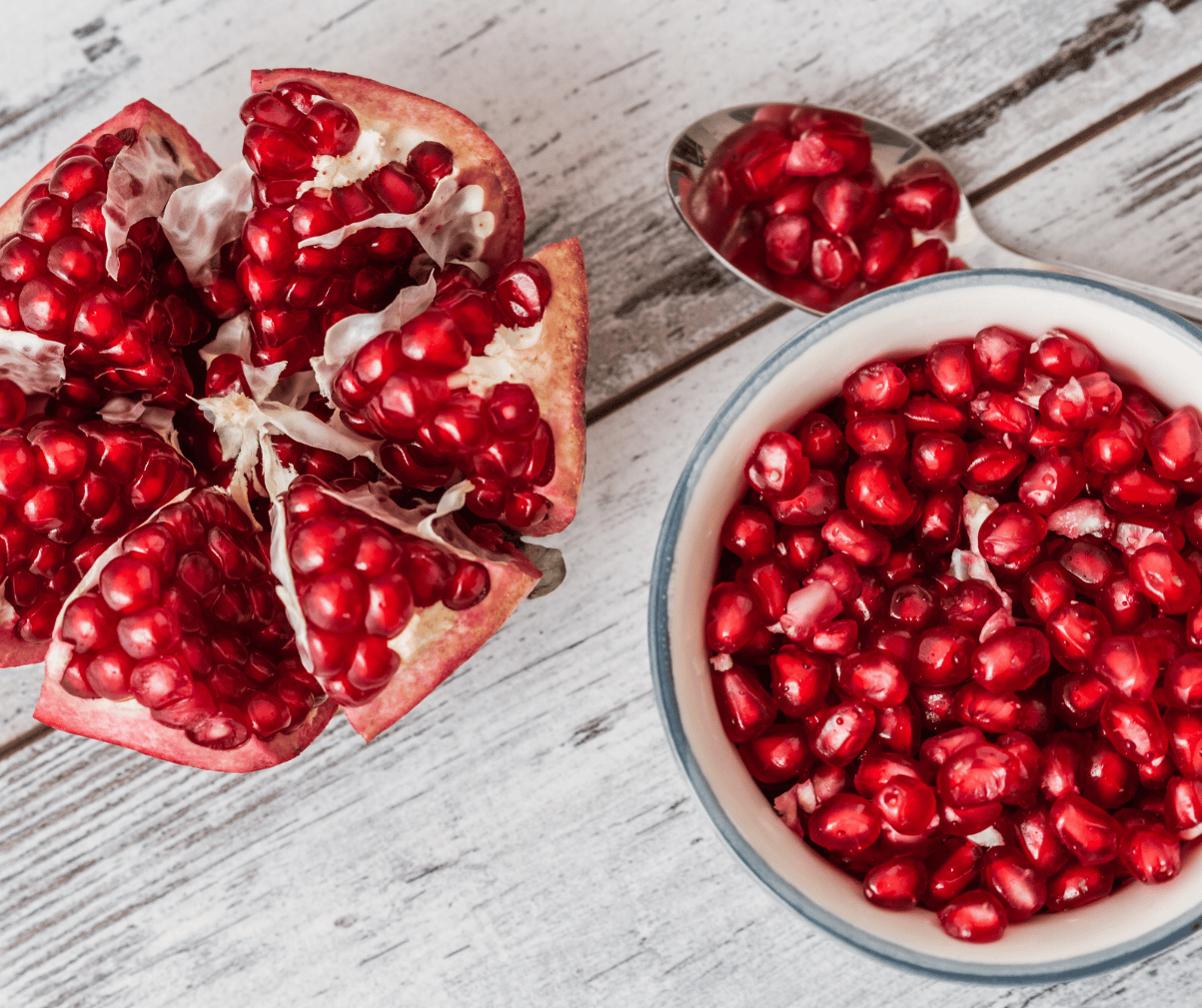 Kuvassa on valkeassa kulhossa granaattiomenan siemeniä sekä vieressä kokonainen avattu granaattiomena