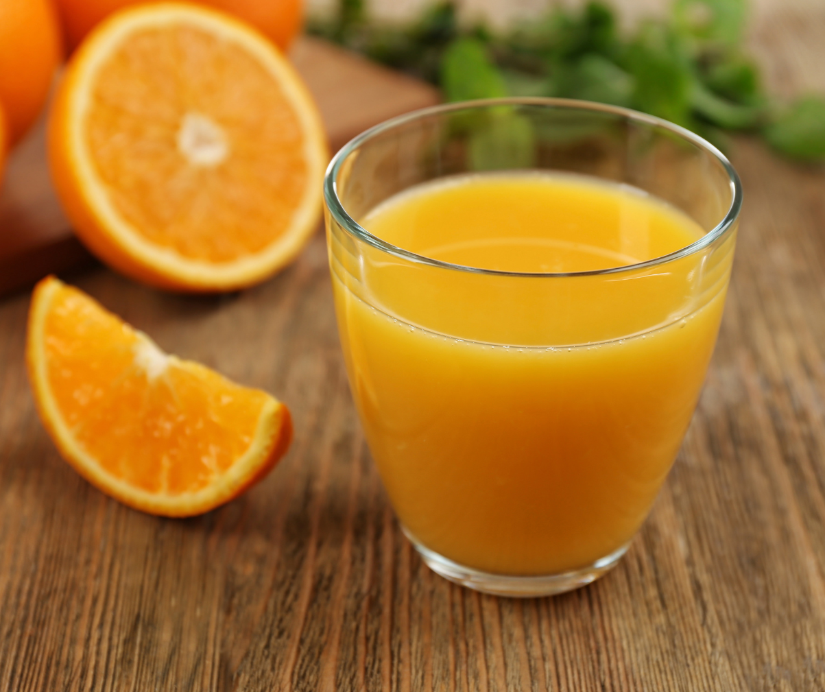 Kuvassa puolikas appelsiini sekä appelsiinilohko ja lasillinen appelsiinimehua