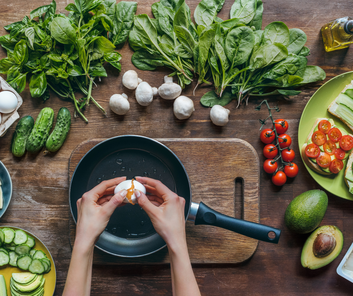 Kuvassa valmistetaan kananmunaa pannulla. Taustalla pöydällä on erilaisia kasviksia.