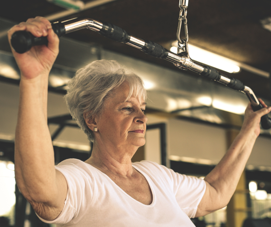 Iäkäs nainen tekee ylävartaloharjoitusta taljalaitteella kuntosalilla.