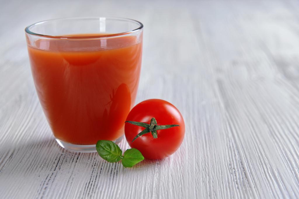 Lasillinen tomaattimehua. Vieressä tuore tomaatti.
