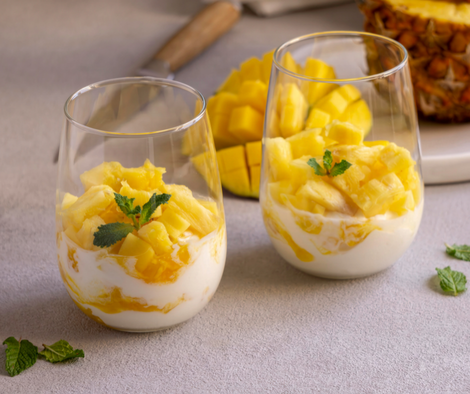 Kulhossa mangosta ja rahkasta koottuja jälkiruokia. Taustalla puolikas mango.