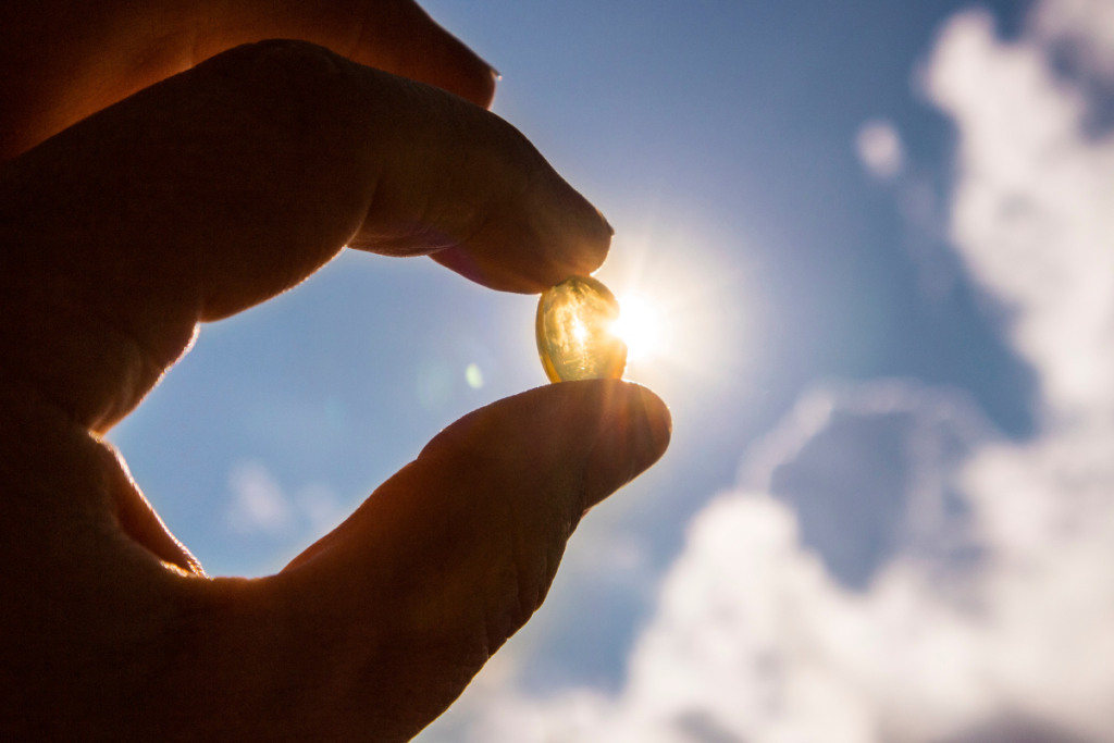 Käsi pitelee vitamiinitablettia vasten aurinkoa.