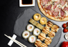 Kivilautasilla erilaisia susheja ja toisella pizzaa. Vieressä soijaa ja puikot.