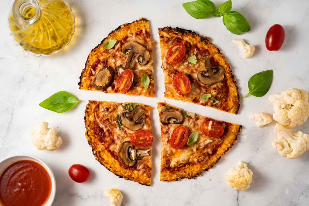 Neljään osaan jaettu pizza. Ulkopuolella basilikaa, valkosipulia ja öljyä.