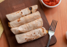 Neljä burritoa leikkuulaudan päällä. Vieressä haarukka ja salsaa.
