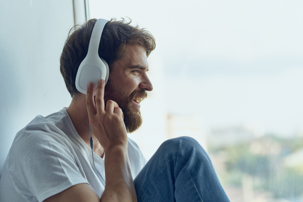 Mies kuuntelee kuulokkeista musiikkia ikkunan äärellä.